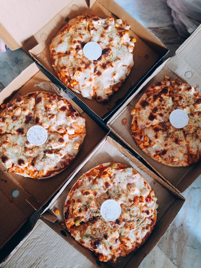 Top view of four cheese pizzas in open cardboard boxes, ready to serve.