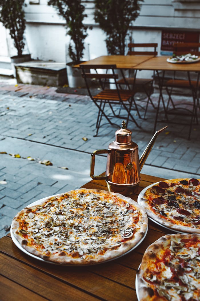 Delicious pizzas served at an outdoor Italian restaurant with a vintage kettle on a wooden table.